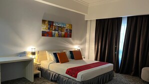A hotel room with a bed, bedside tables, a desk, a chair, a painting on the wall, and a window with curtains. - Hotel Seri Malaysia Genting Highlands (Genting Highlands)