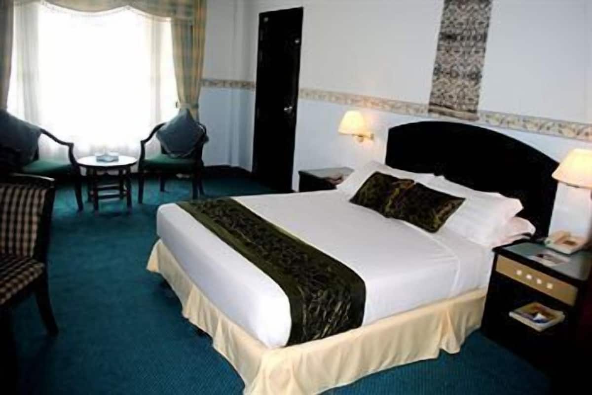 A hotel room with a large bed, two bedside tables, a chair, a small table, and a window with curtains.