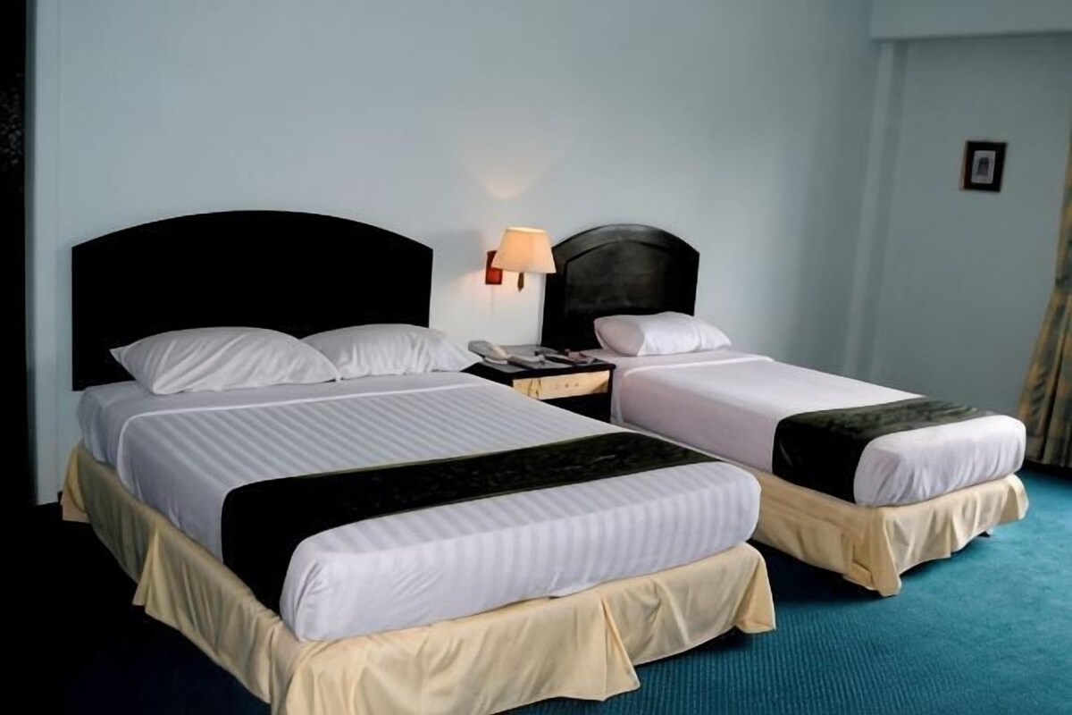 Habitación de hotel con dos camas, una mesita de noche con lámpara y alfombra azul.