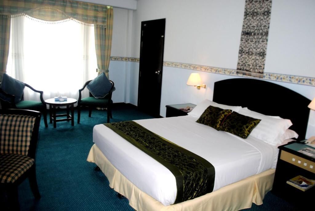A hotel room with a large bed, a desk with a chair, a lamp, and a door.
