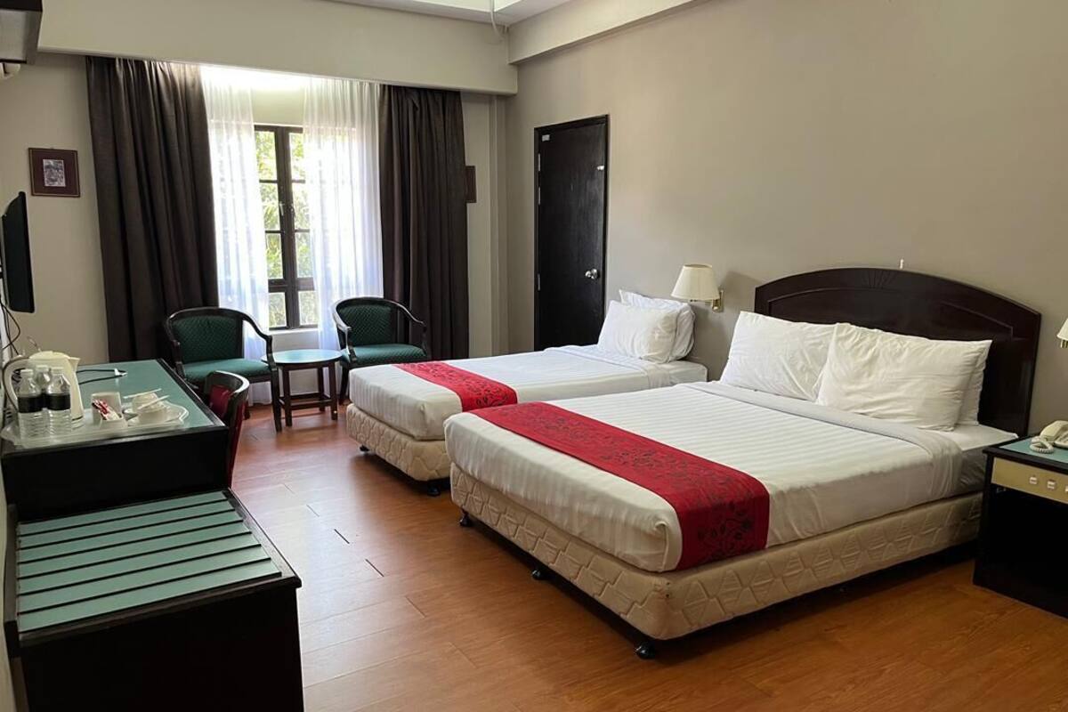 A hotel room with two beds, a desk with a telephone, a chair, and a window with curtains.