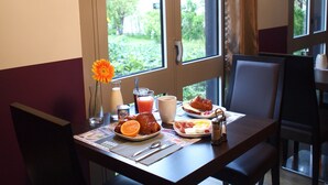Een ontbijttafel met eten op een bord, een glas sap, een beker en een vaas met een bloem.