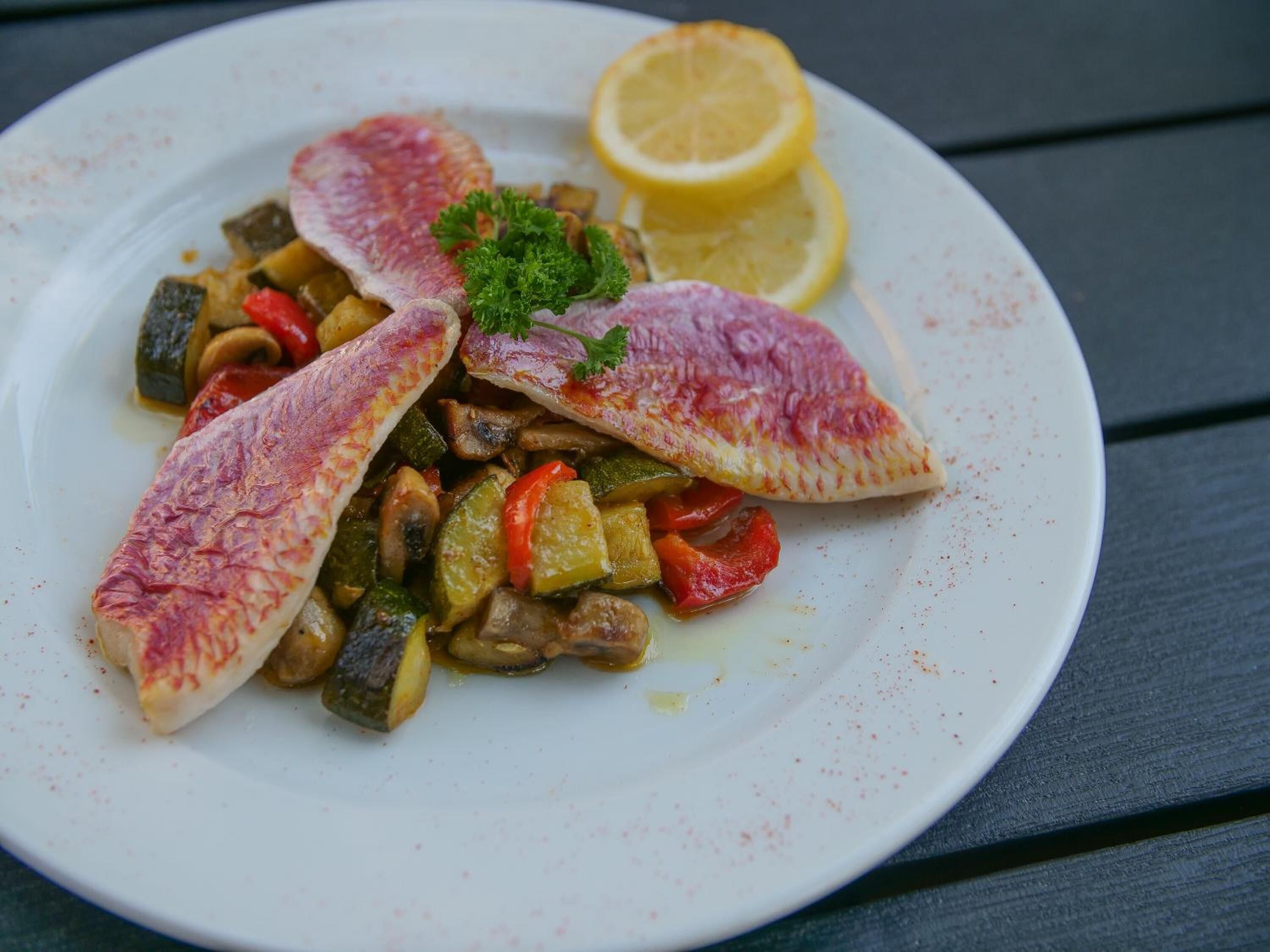 A plate of fish fillets with vegetables and a lemon wedge.