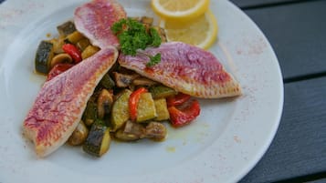 A plate of fish fillets with vegetables and a lemon wedge.