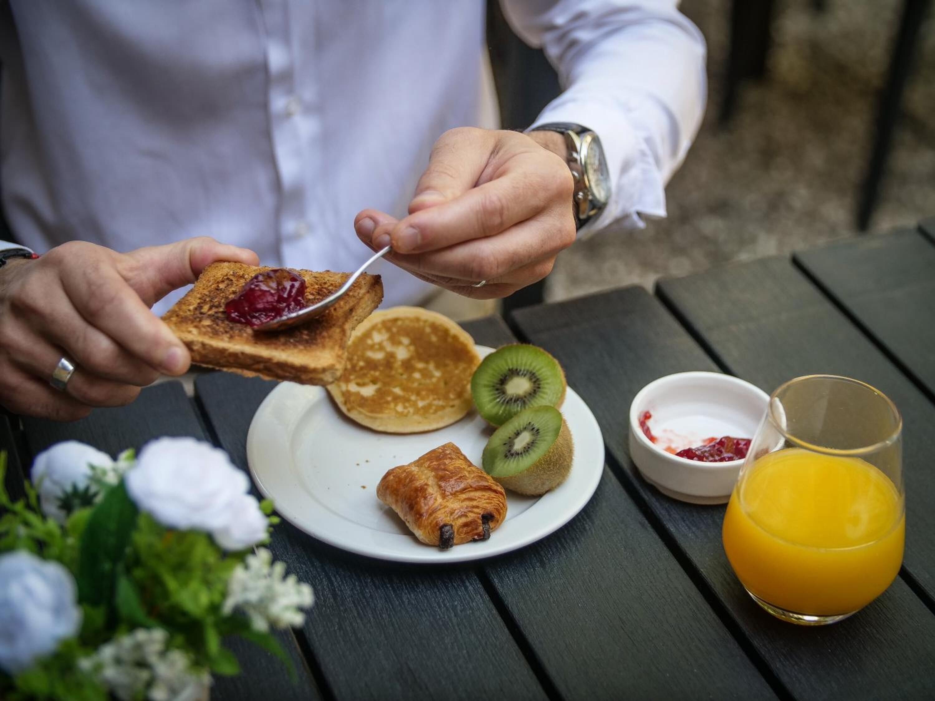 Une table dressée pour le petit-déjeuner, avec des toasts, des crêpes, des tranches de kiwi, un croissant et du jus d’orange.