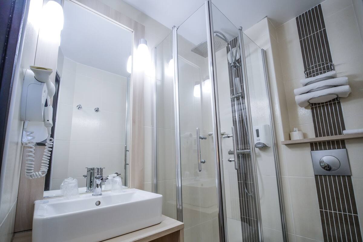 Ein modernes Badezimmer mit einer gläsernen Duschkabine, einem weißen Waschbecken und einem Handtuchhalter.