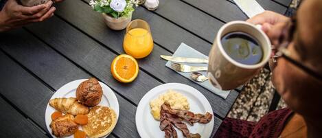 Un desayuno con platos de comida, una taza de café y un vaso de zumo de naranja sobre una mesa de madera.