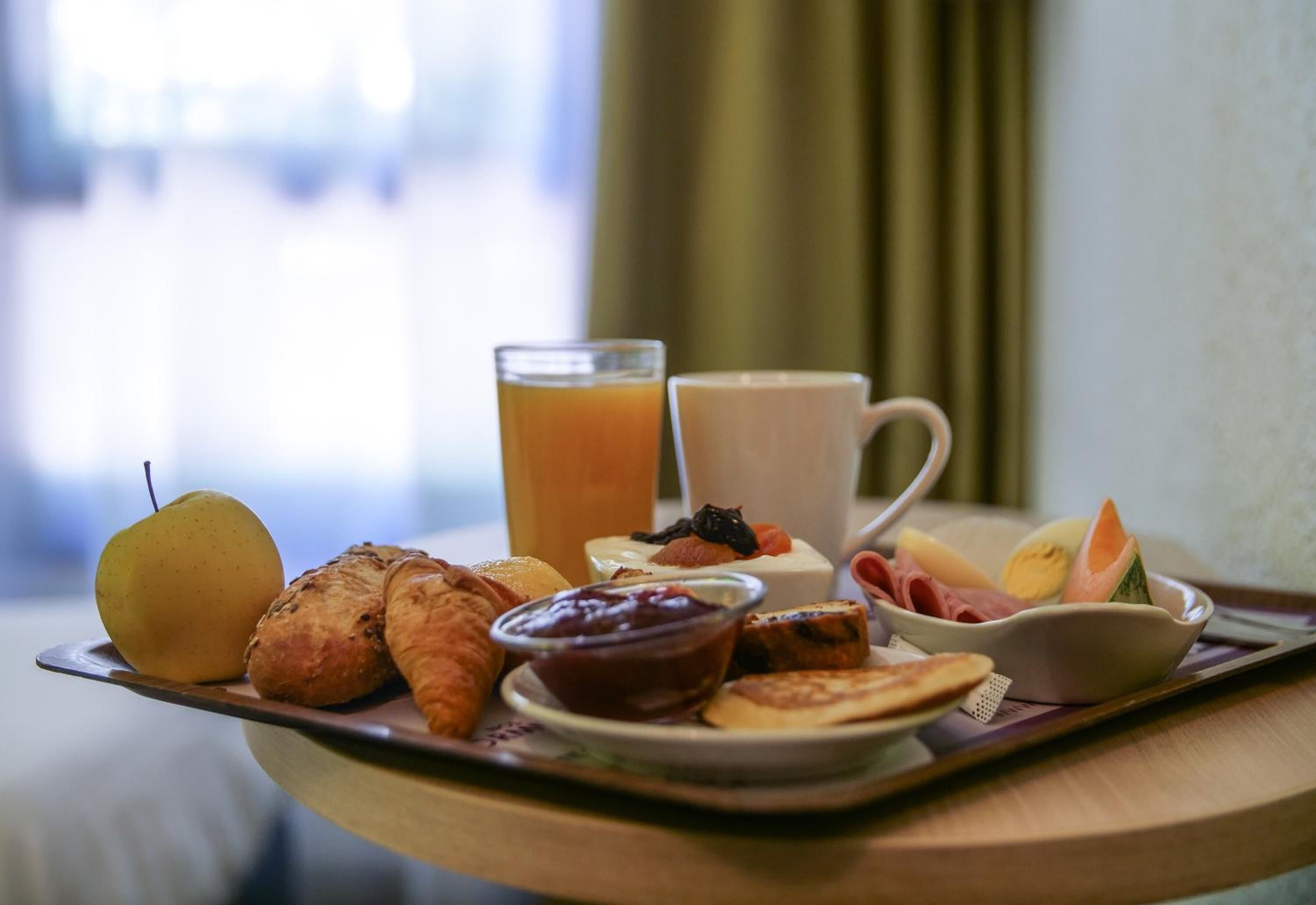 A breakfast tray with croissants, a pear, a glass of orange juice, a cup, and a bowl of fruit on a wooden table.