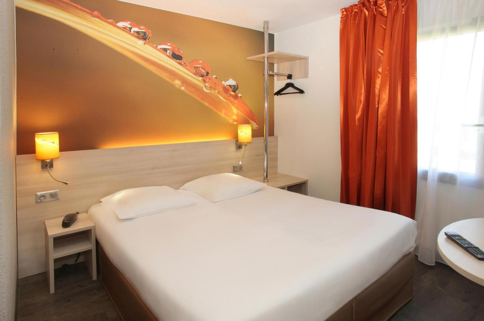 Et hotelværelse med en stor seng, sengeborde med lamper, et skrivebord, et knagered og et vindue med orange gardiner.