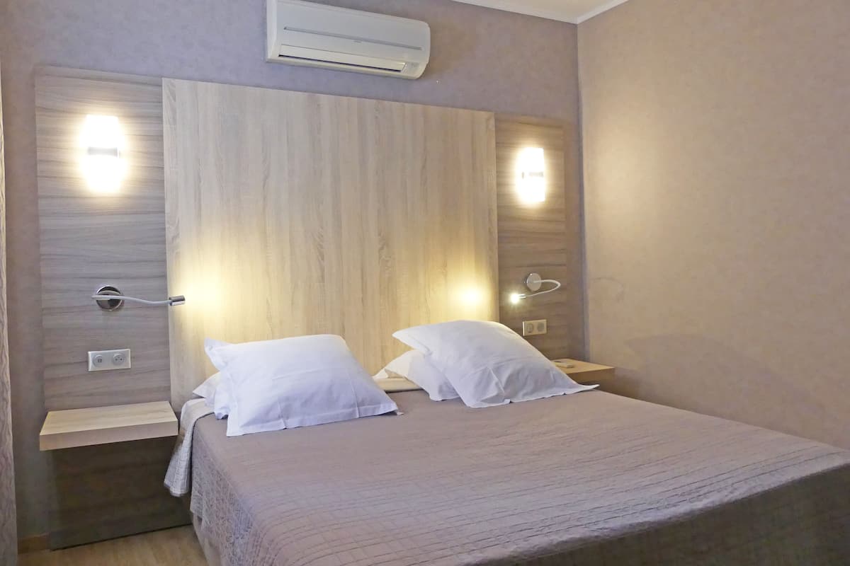 A bedroom with a bed, bedside tables, an air conditioner, and wall-mounted lights.