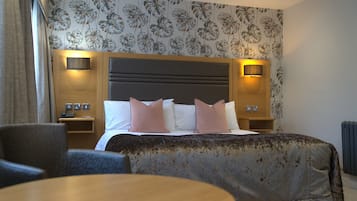 Ein Hotelzimmer mit einem großen Bett, zwei Nachttischen mit Lampen, einem runden Tisch und floralem Wandpapier.