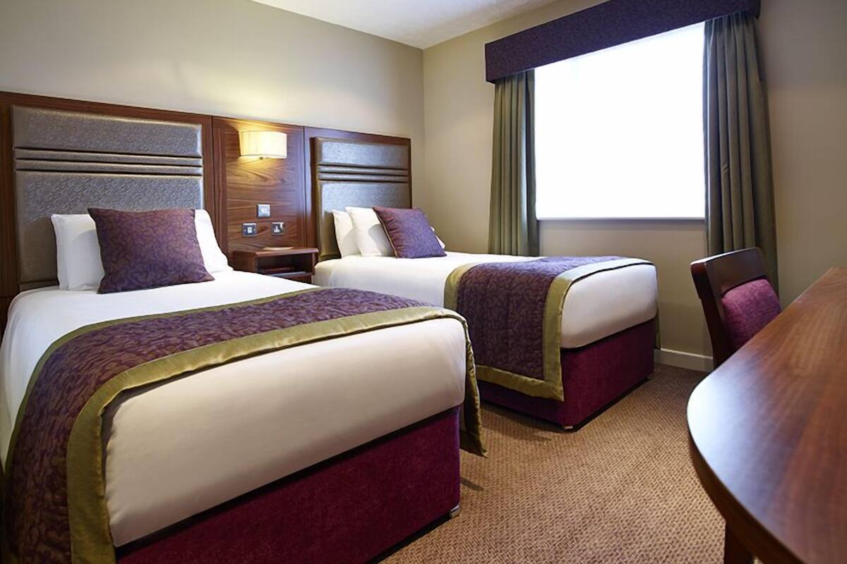 Habitación de hotel con dos camas, un escritorio y una ventana con cortinas.