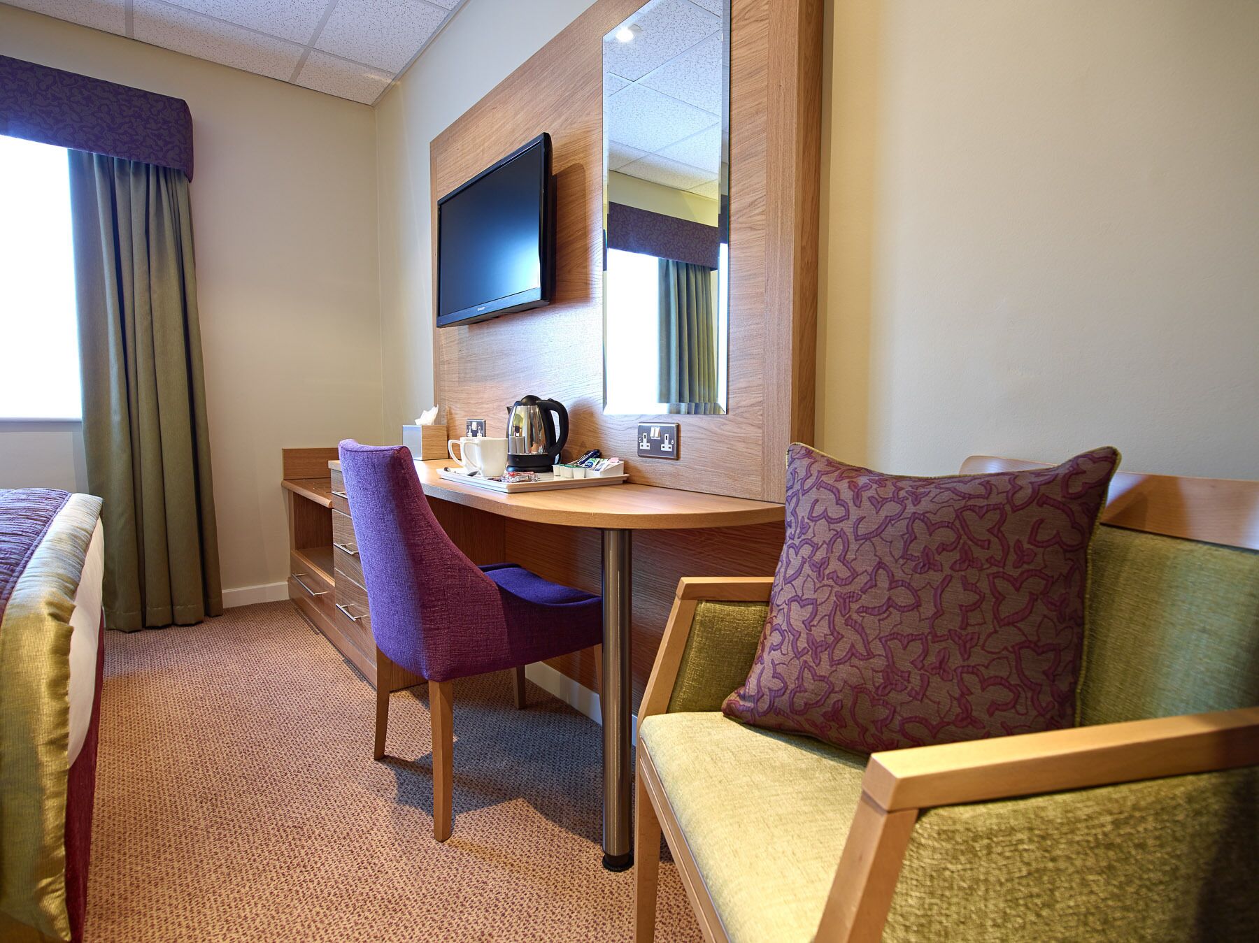 A hotel room with a bed, a desk with a chair, a television, and a mirror.