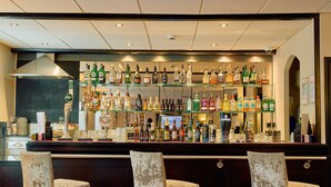 Uma área de bar com várias prateleiras de garrafas de bebidas, um balcão e três cadeiras.