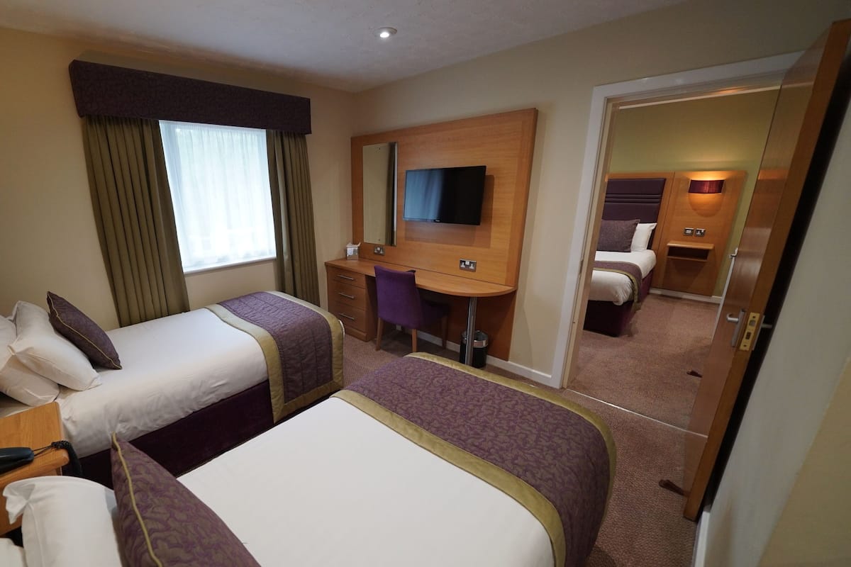 Habitación de hotel con dos camas, un escritorio, una silla, un televisor y un espejo.