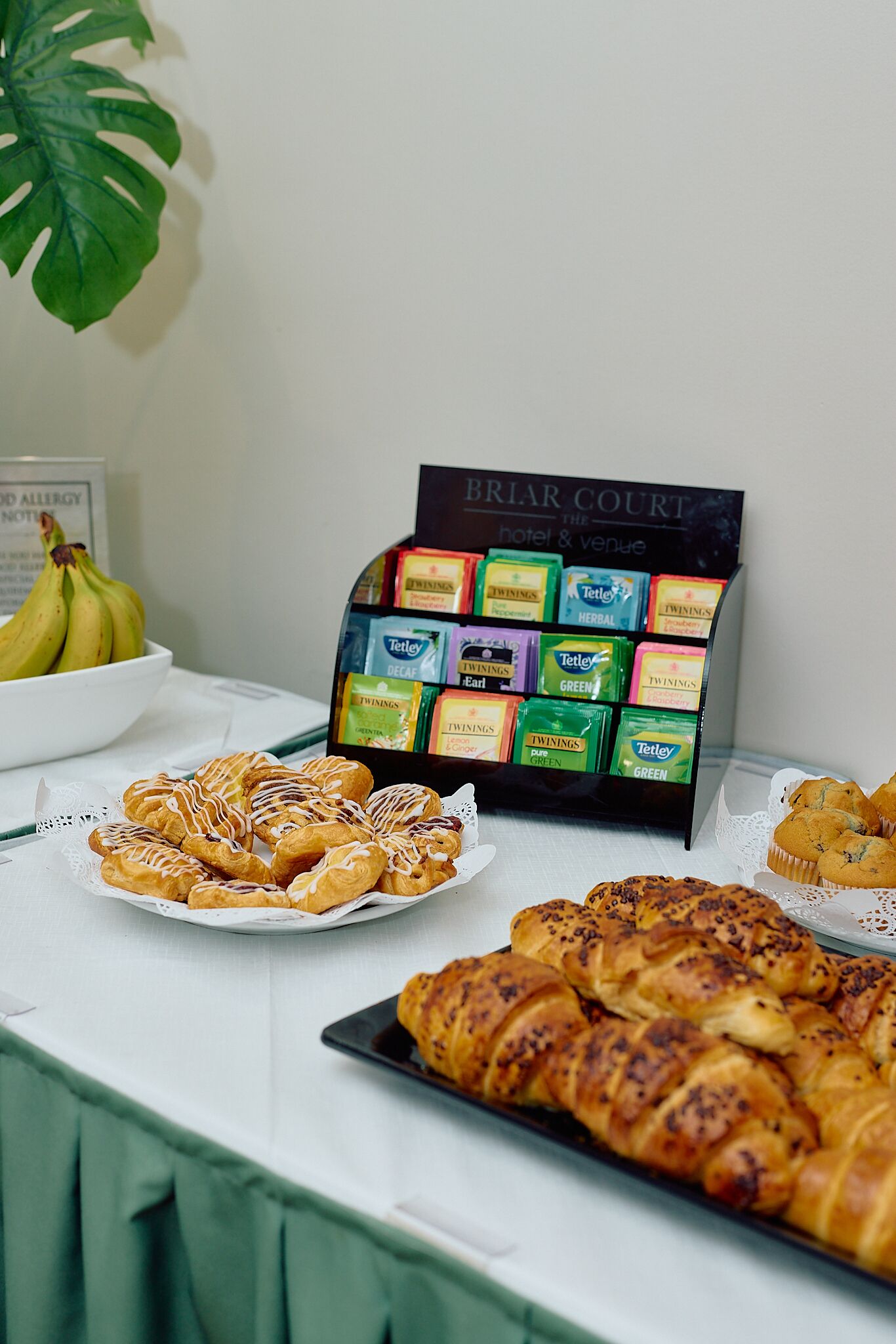 A buffet table with pastries, a fruit bowl, and a display of herbal tea bags.