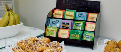 A buffet table with pastries, a fruit bowl, and a display of herbal tea bags.