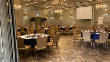 Un salón de conferencias con varias mesas y sillas, candelabros y una pantalla de proyector.