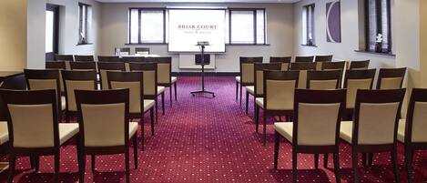 A conference room with rows of chairs, a projector screen, and a carpeted floor.