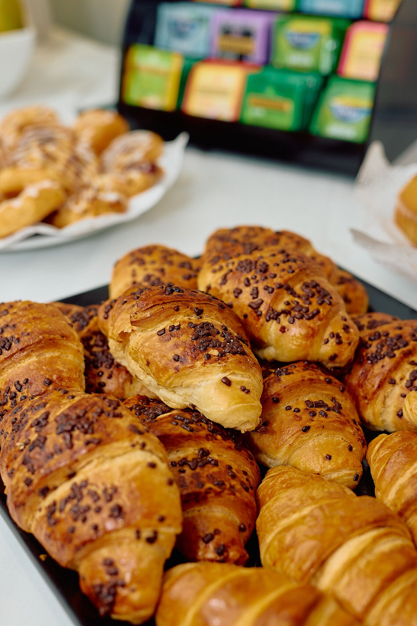 A tray of golden-brown croissants with chocolate chips, arranged on a white surface.