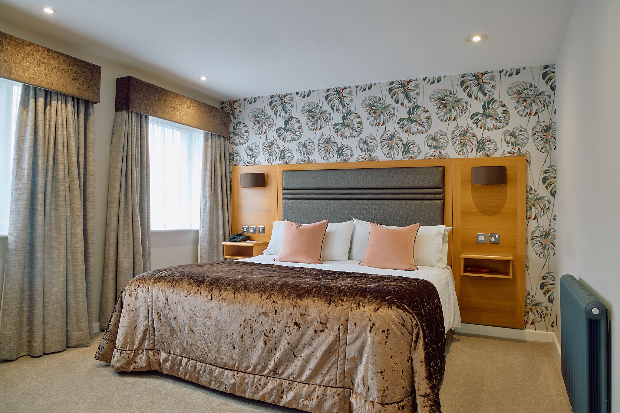 Habitación de hotel con una cama grande, un cabecero de madera, una mesita de noche y una pared con estampado floral.