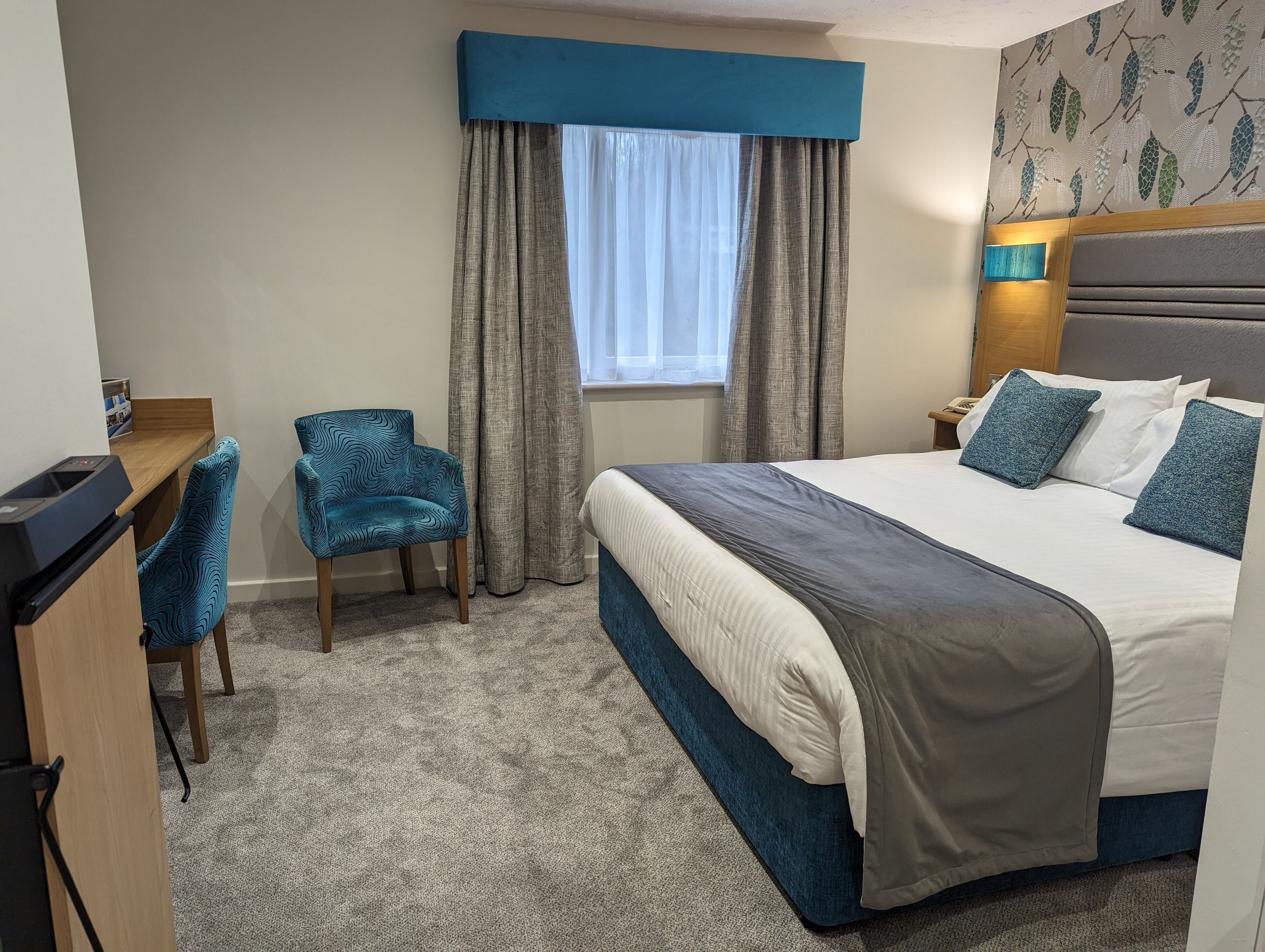 Habitación de hotel con cama, escritorio, silla y ventana con cortinas.