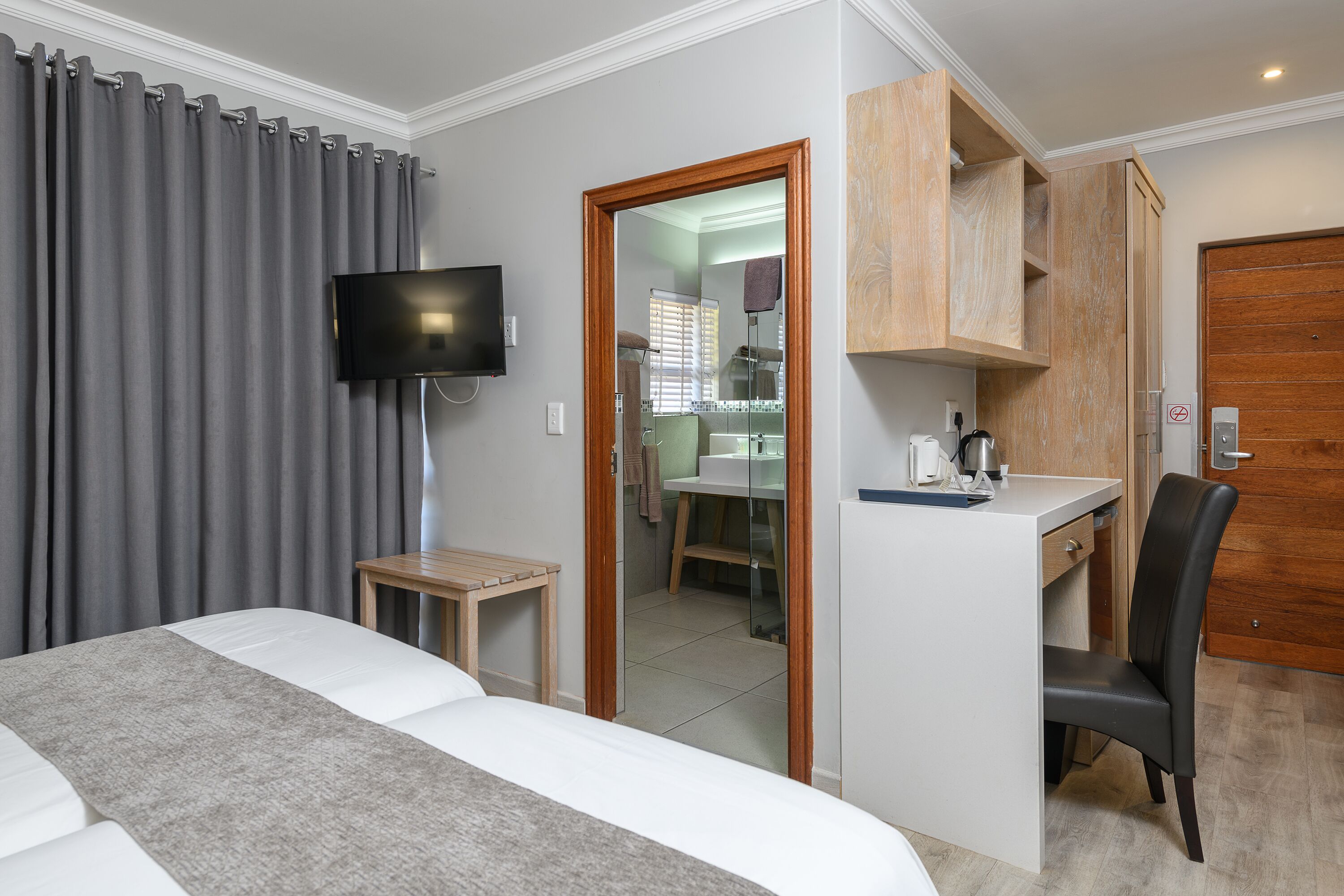 Habitación de hotel con cama, escritorio, silla, televisión y baño visible a través de una puerta abierta.