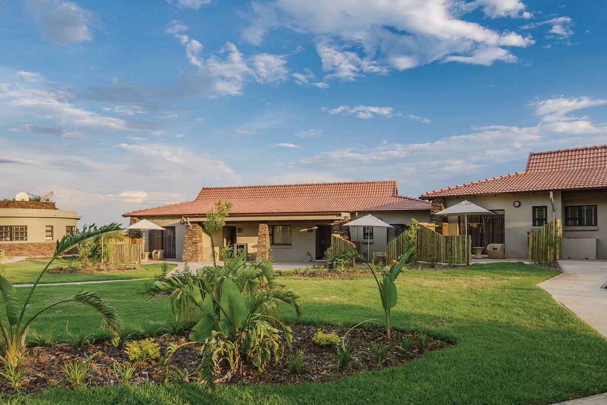 A residential area with houses featuring red-tiled roofs and stone walls, surrounded by well-maintained lawns and tropical plants.