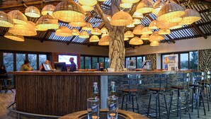 A bar area with a wooden counter, multiple stools, and hanging lamps. - The Kingdom Resort (Moses Kotane)