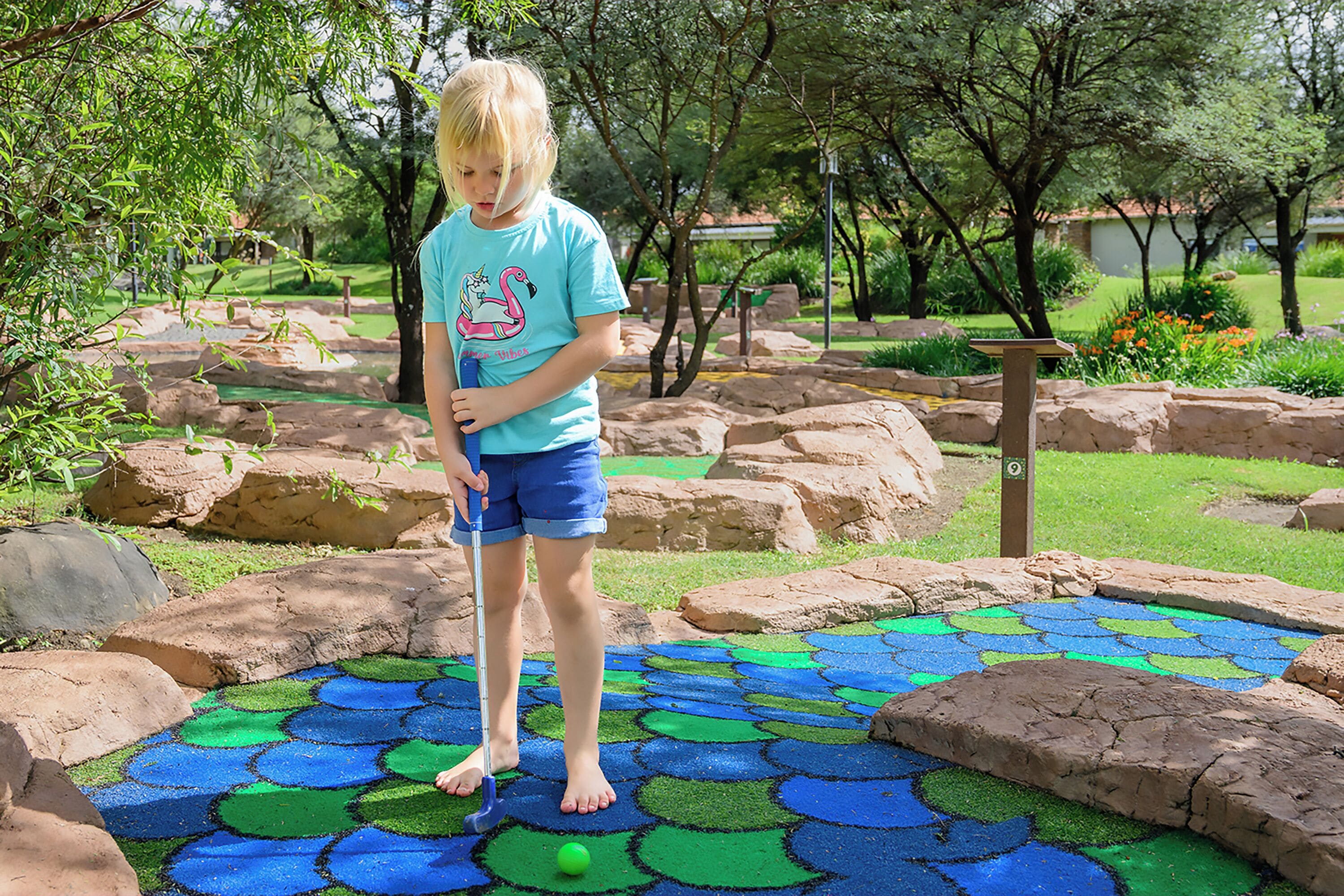 A child playing on a colorful outdoor play area with rocks and greenery.