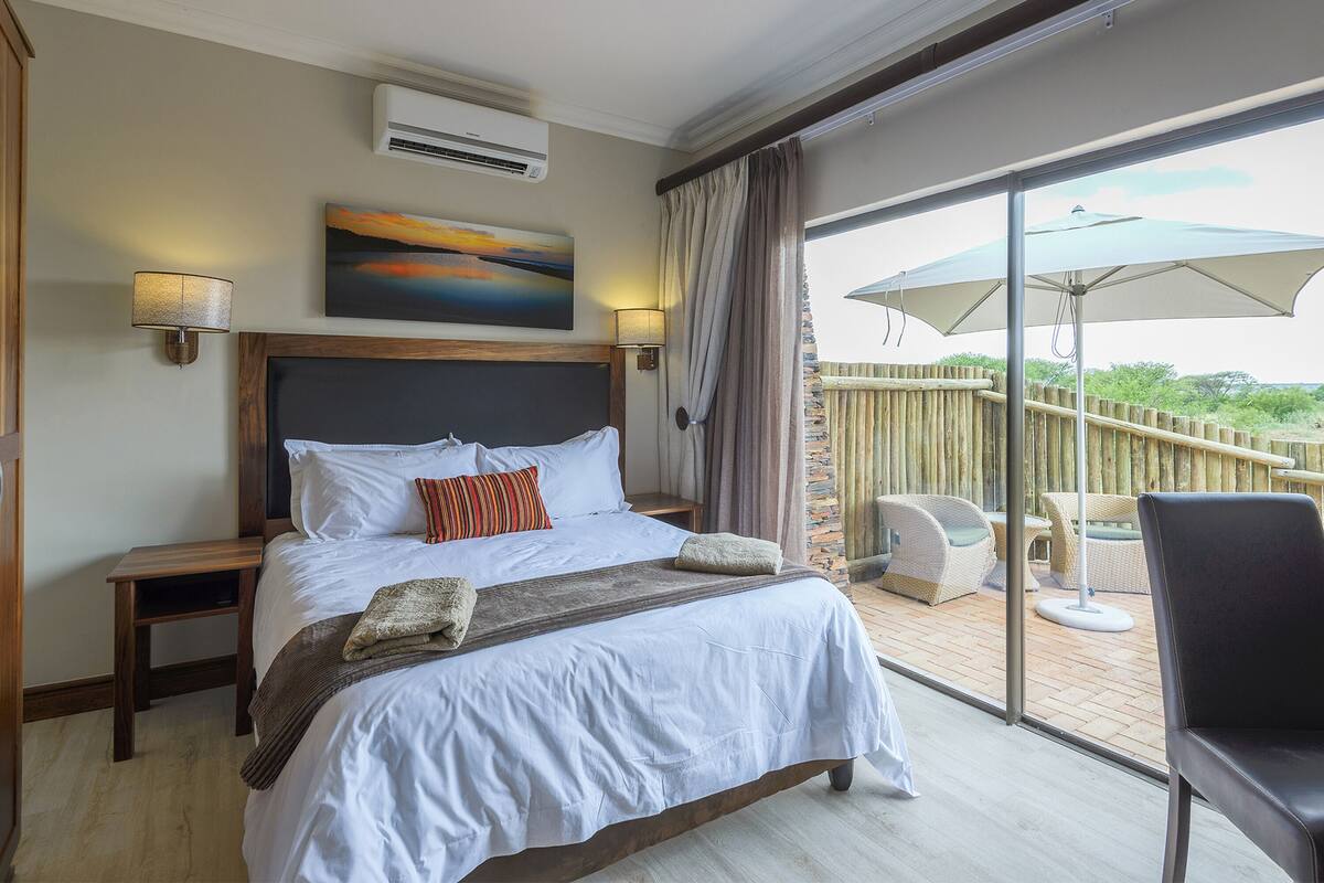 A hotel room with a large bed, a view of the outdoors, and a balcony with outdoor furniture.