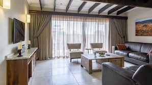 A living room with a wooden ceiling, a sofa, chairs, a coffee table, and a TV on the wall. - The Kingdom Resort (Moses Kotane)