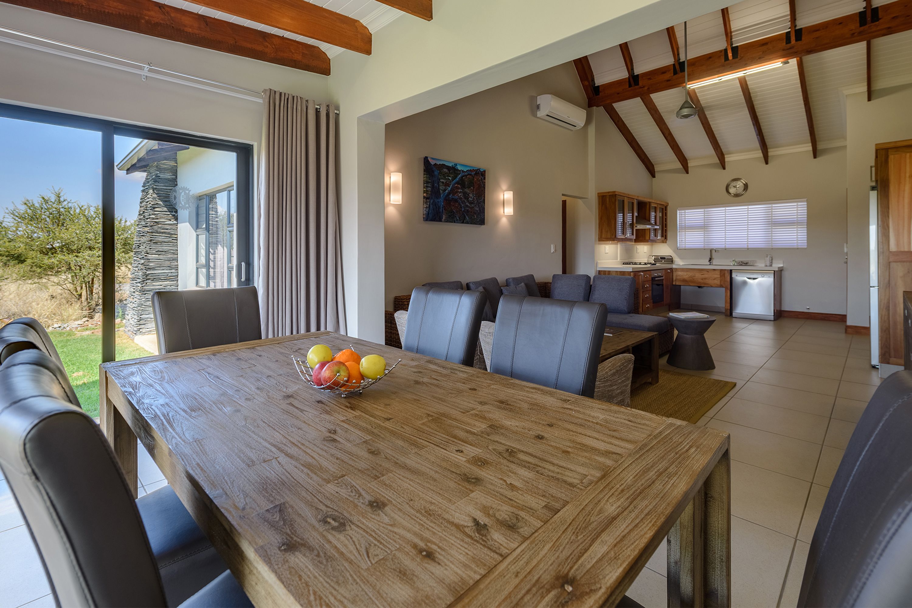 Ein geräumiger Wohnbereich mit einem Holzespeisetisch, grauen Sofas und einer Küche im Hintergrund.