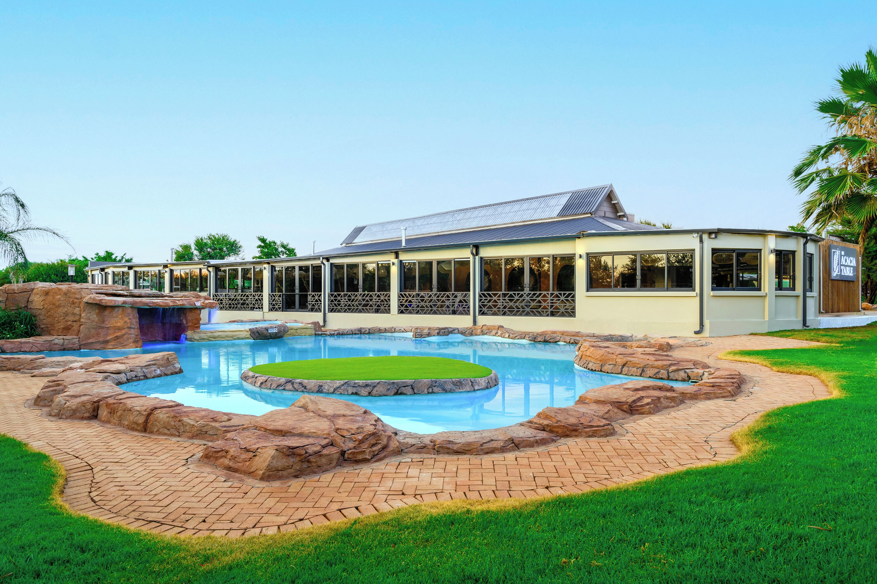A modern hotel with a swimming pool, a covered area, and a well-maintained lawn.