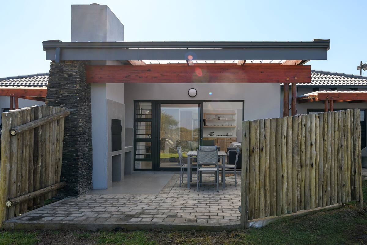 A modern house with a patio area, a wooden fence, and a stone wall.