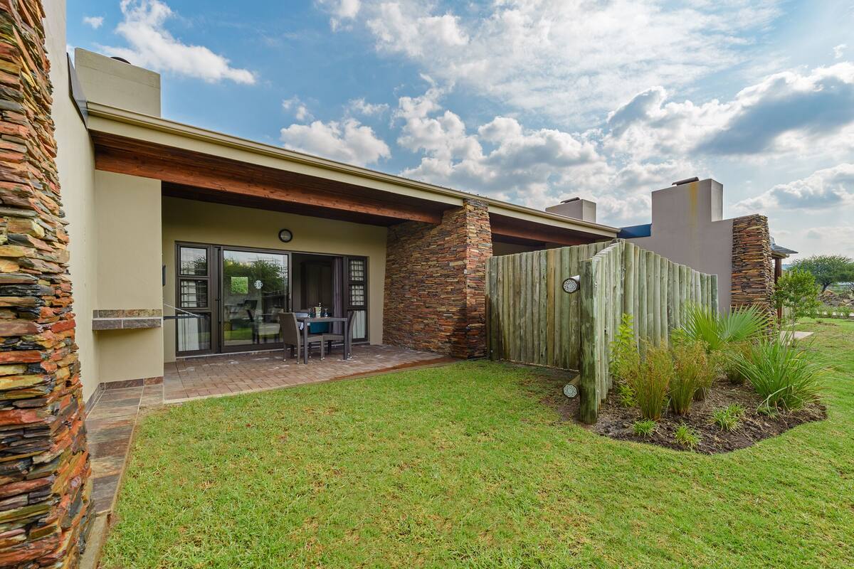 A modern house with a stone exterior, a wooden deck, and a well-maintained lawn.