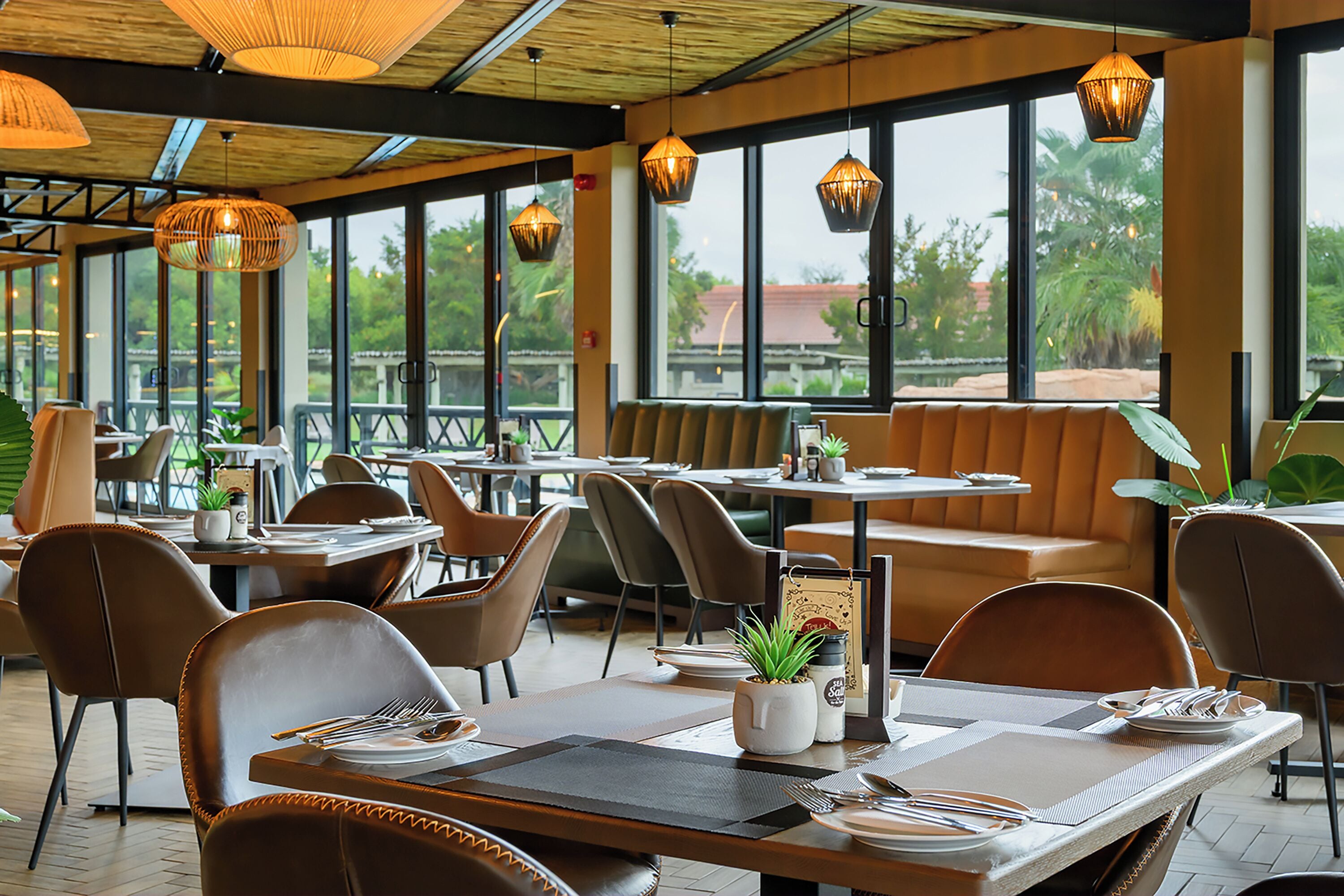 A restaurant with tables and chairs, large windows, and hanging lights.