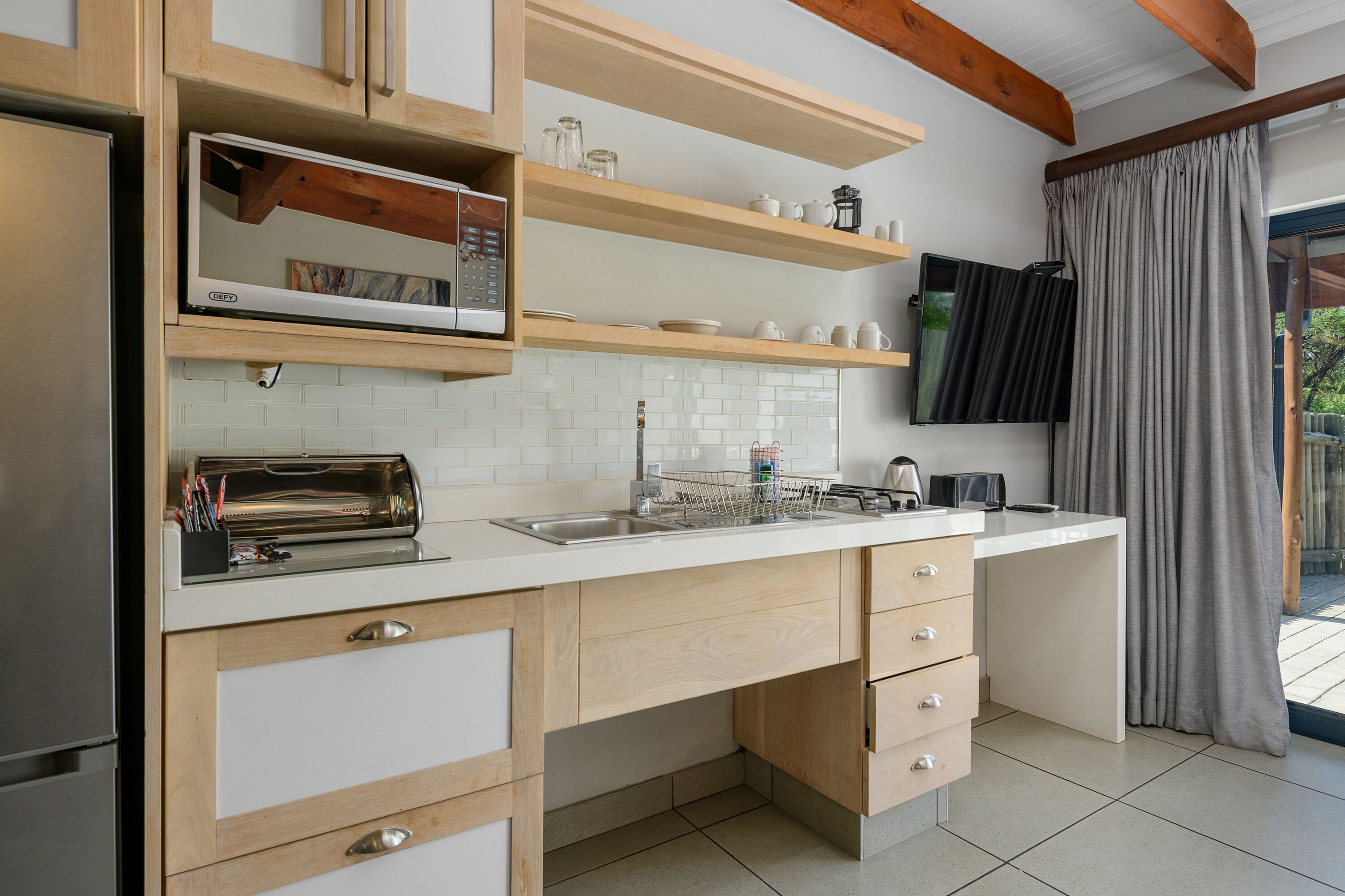 Een moderne keuken met houten kastjes, een ingebouwde magnetron, een broodrooster en een flatscreen televisie aan de muur.
