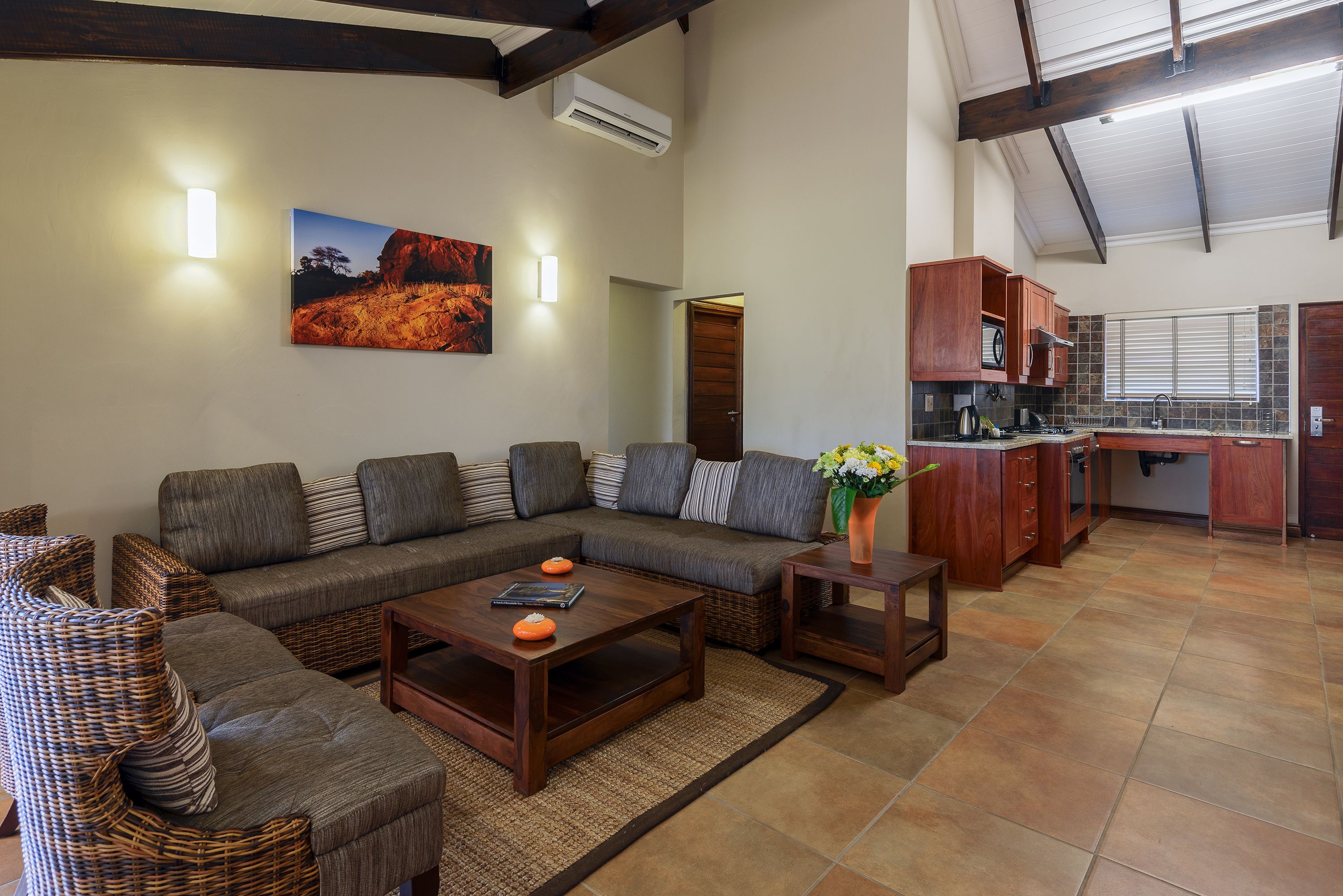 A living room with a sectional sofa, a coffee table, and a kitchen area with wooden cabinets and a window.