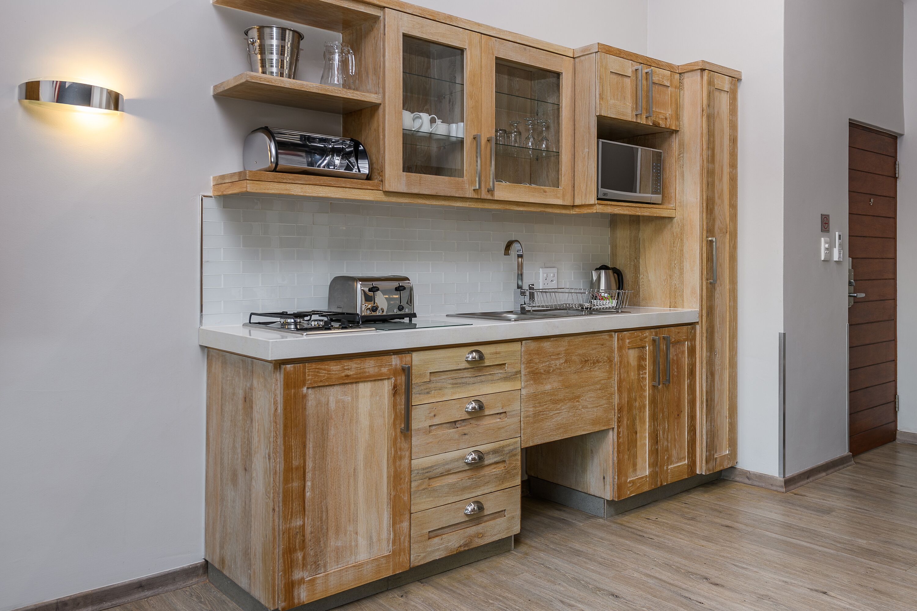 A kitchen with wooden cabinets, a stainless steel toaster, a microwave, and a sink.