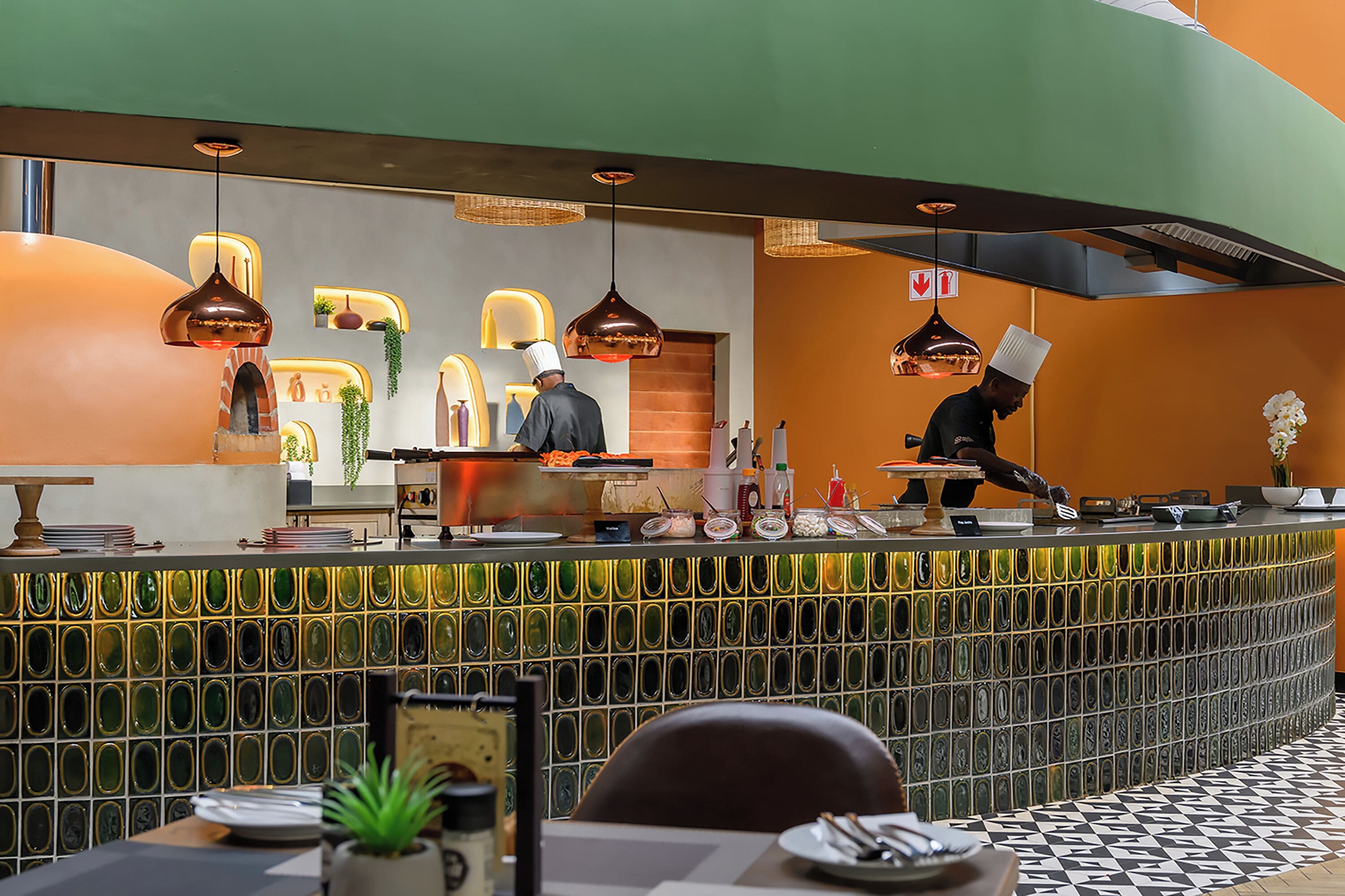 A restaurant with a curved counter, hanging pendant lights, and a tiled backsplash.