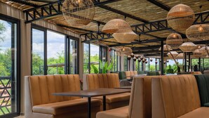 A restaurant with leather booths, large windows, and wicker pendant lights. - The Kingdom Resort (Moses Kotane)