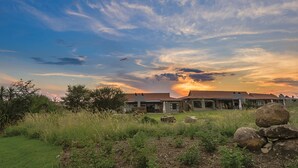 A house with a red roof, surrounded by a grassy area with rocks and trees. - The Kingdom Resort (Moses Kotane)