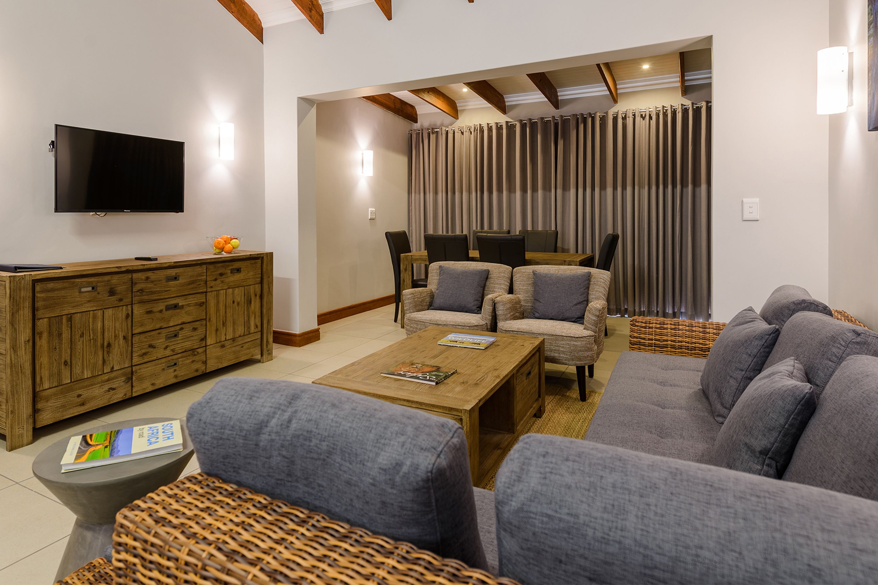 Una sala de estar moderna con televisor de pantalla plana, mueble de madera, sofás grises y una mesa de centro.