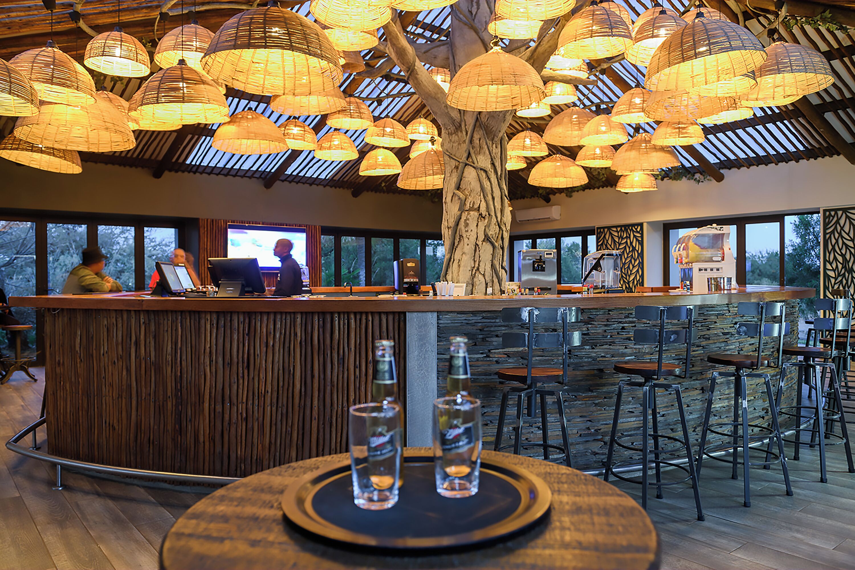 A bar area with a wooden counter, bar stools, and hanging lamps.