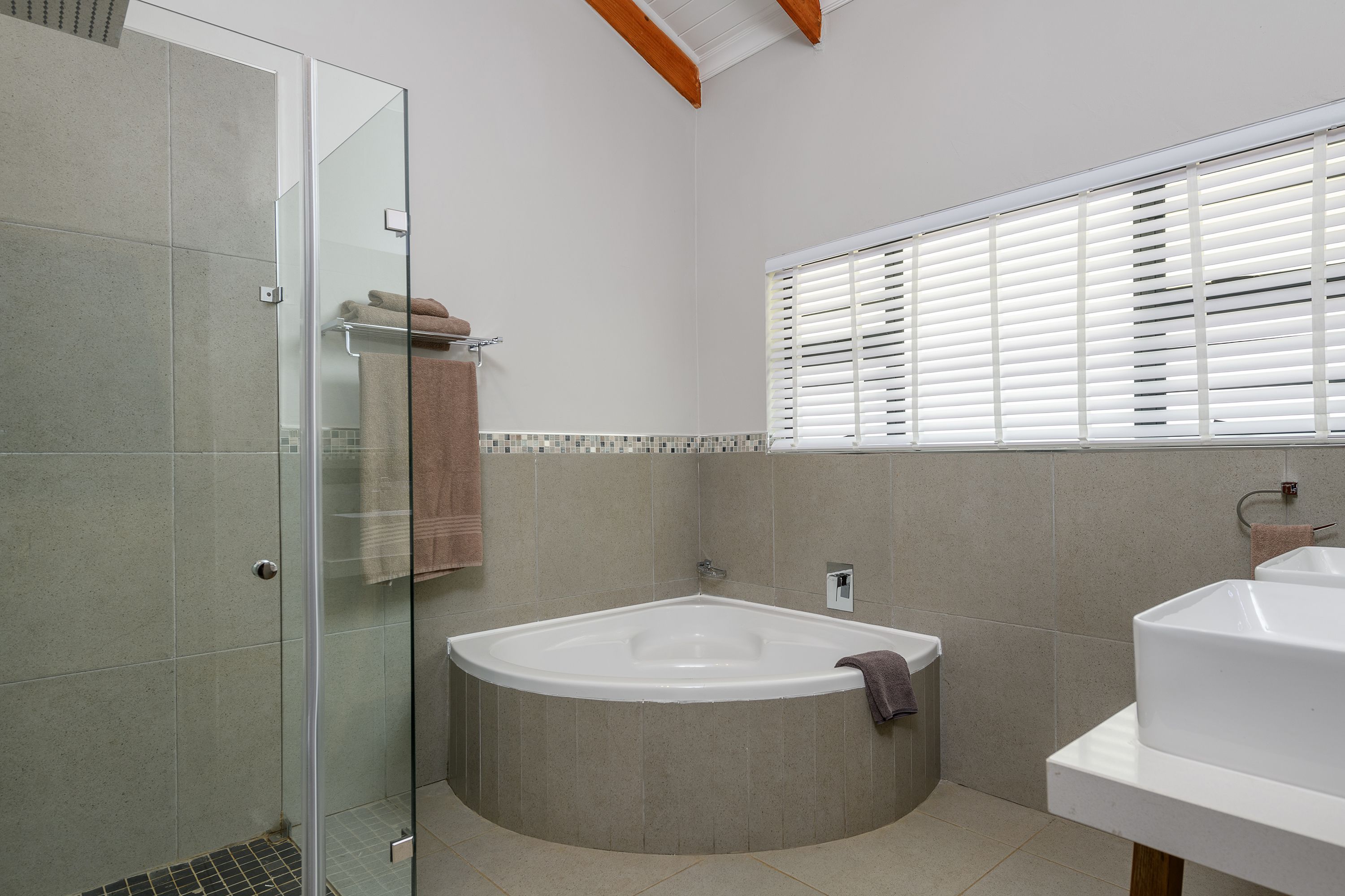 A modern bathroom with a glass shower enclosure, a freestanding bathtub, and a window with blinds.