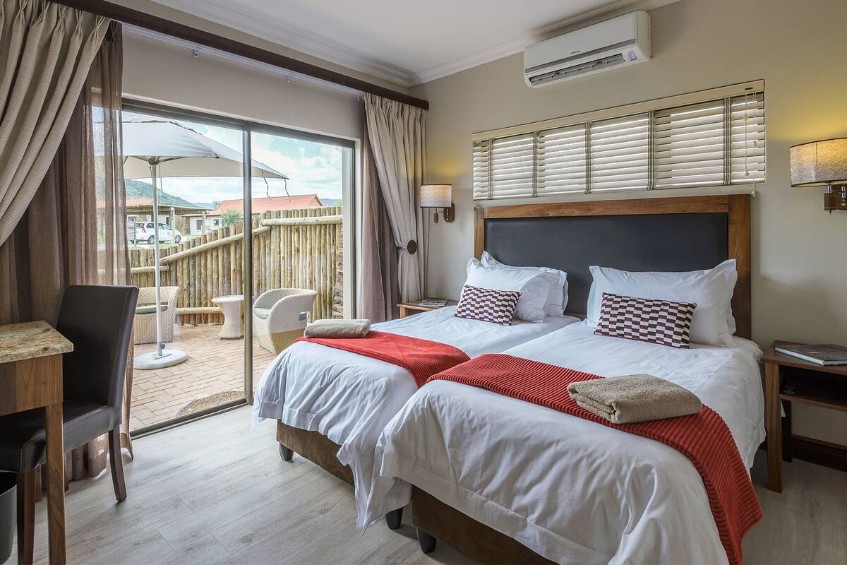 A hotel room with two beds, a desk, and a view of the outside.
