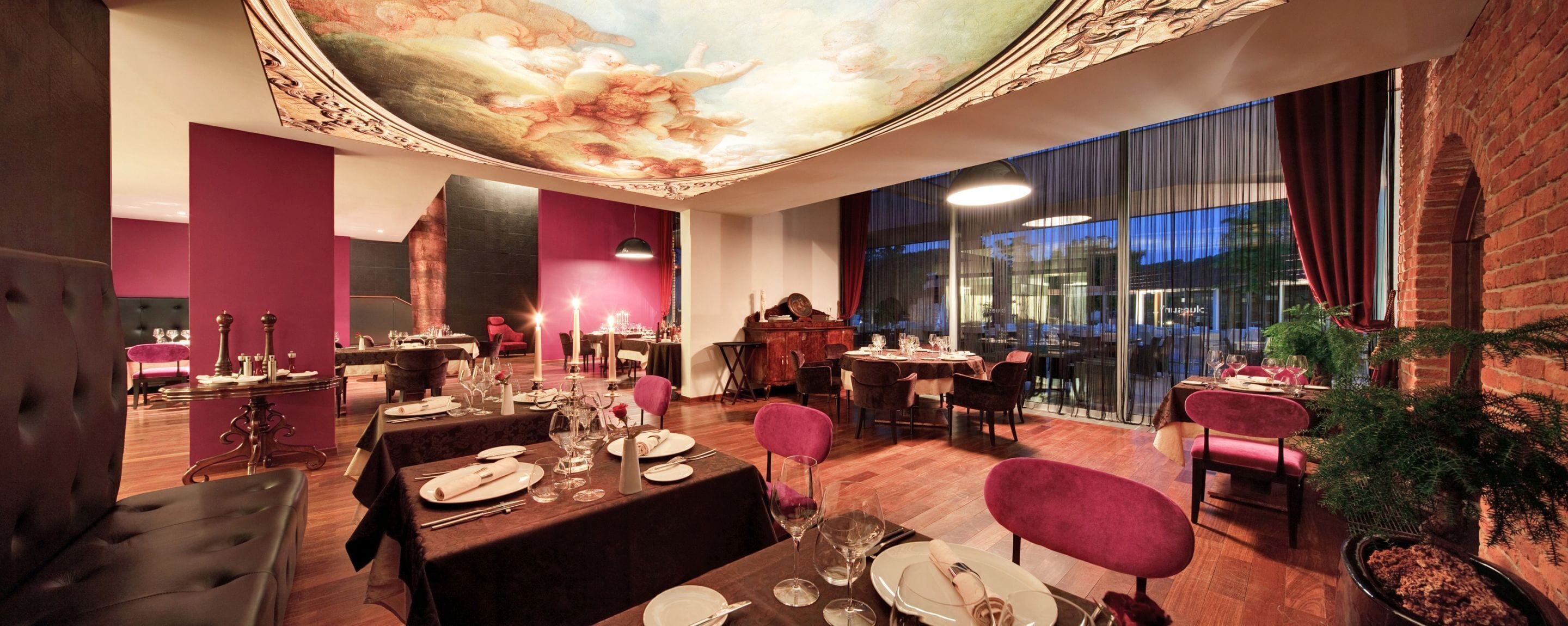 Un restaurante con techo alto, diseño ornamental en el techo y vistas a la ciudad a través de amplias ventanas.