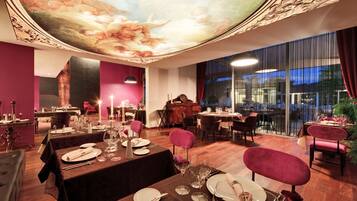 Un restaurante con techo alto, diseño ornamental en el techo y vistas a la ciudad a través de amplias ventanas.