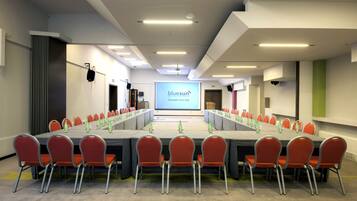 A conference room with a long table, red chairs, and a screen displaying 'bluesun hotel kai'.